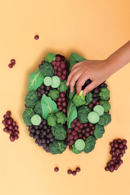 a hand building a brain out of fruits and vegetables