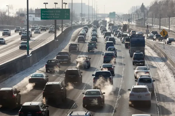 cars driving down highway in the winter. a lot of exhaust is visible